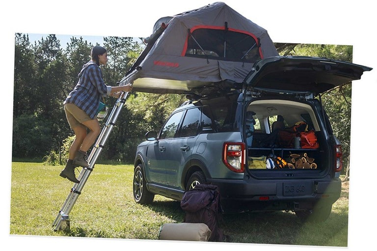 A 2025 Ford Bronco® Sport shown with a tent on the roof and a young woman standing on a ladder